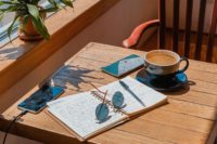 a copy book, sunglasses, and a cup of coffee on the table