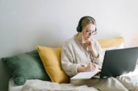 a girl is sitting on a bed with her laptop